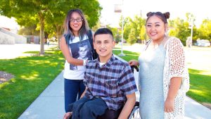 3 students on campus 2 standing and one in a wheelchair