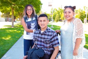 3 students on campus 2 standing and one in a wheelchair