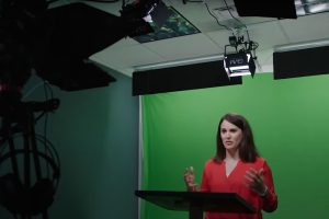 Woman at podium in front of green screen.