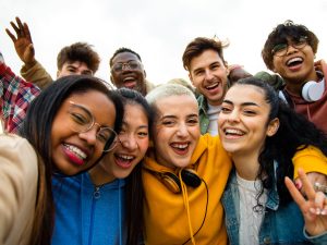 Group of multiracial teen college friends having fun outdoors. Happy people taking selfie. Gen z, friendship and technology concept.